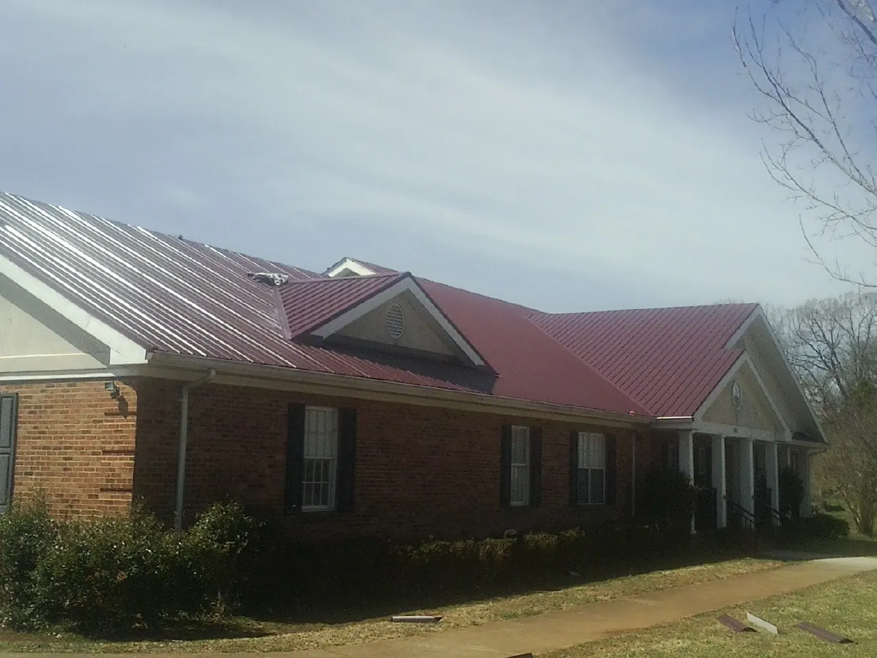 Red metal roof with gabled entries on a long brick building, from a Hail Damage Roof Repair job in Hume